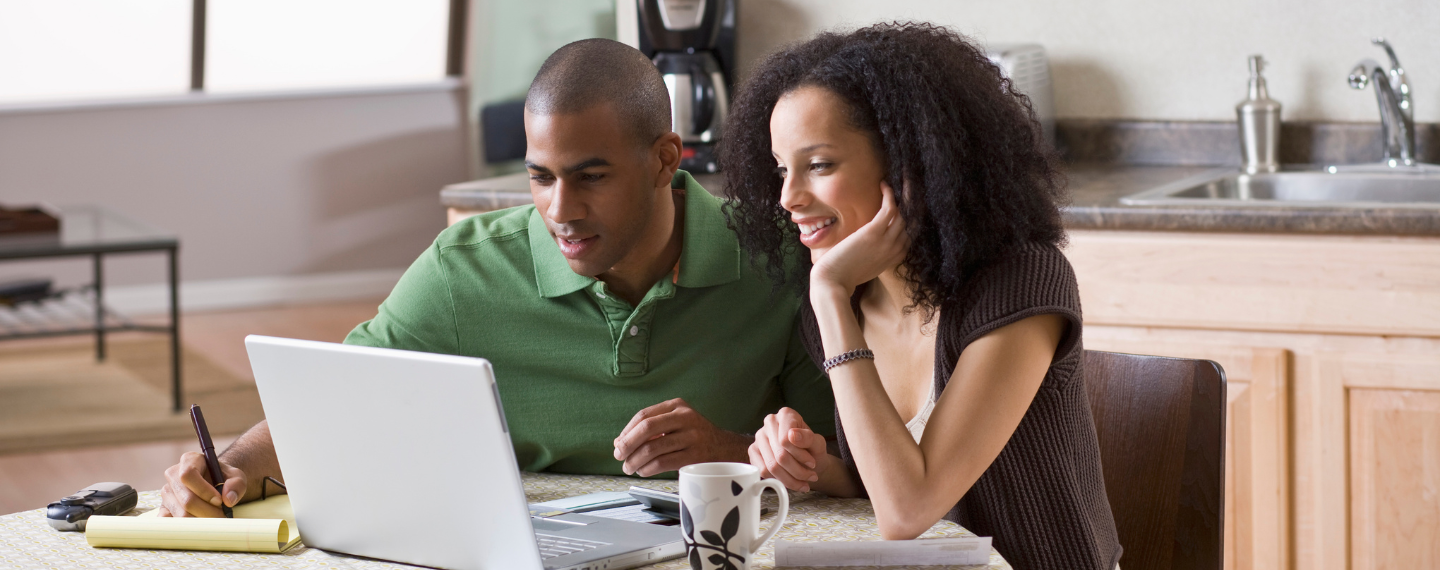 Woman and man sit at table looking at computer screen