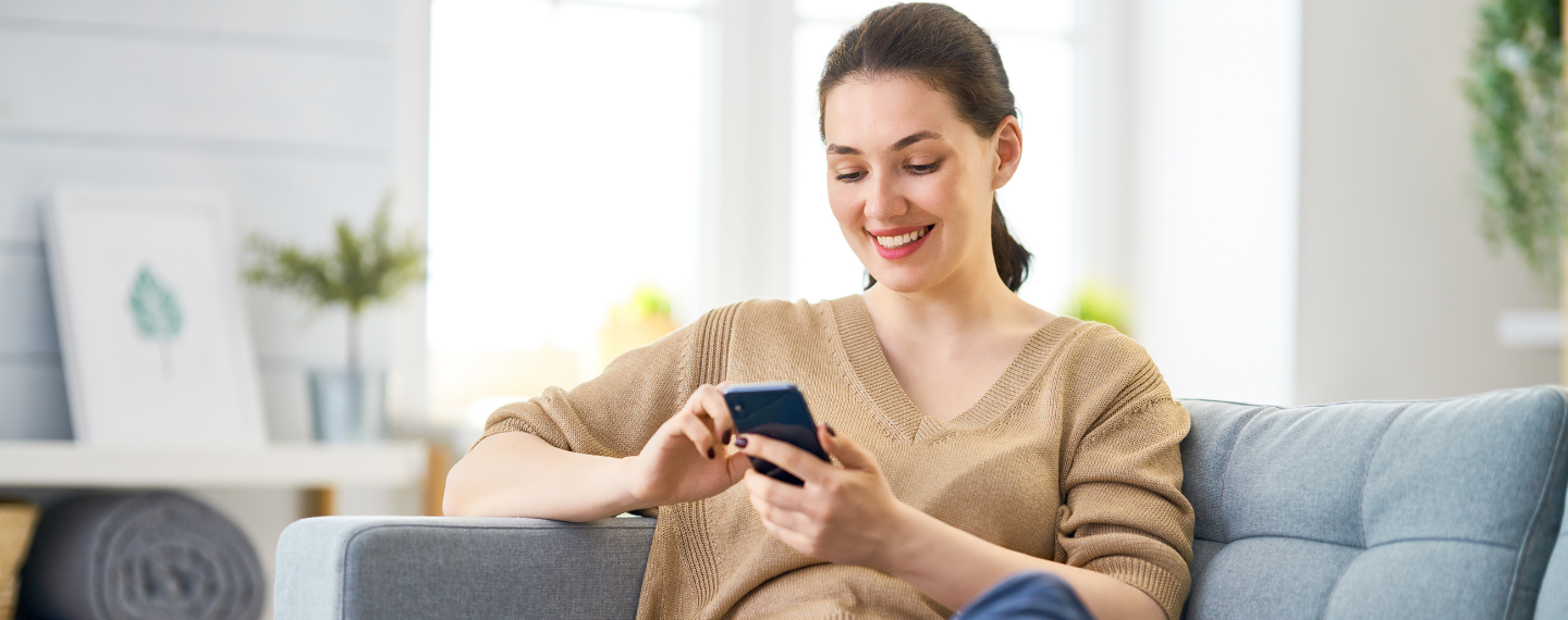Woman smiling sits on couch looking at phone