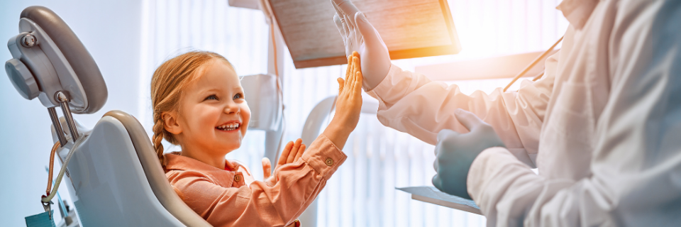 Child on a dentist chair smiles and gives the dentist a high five