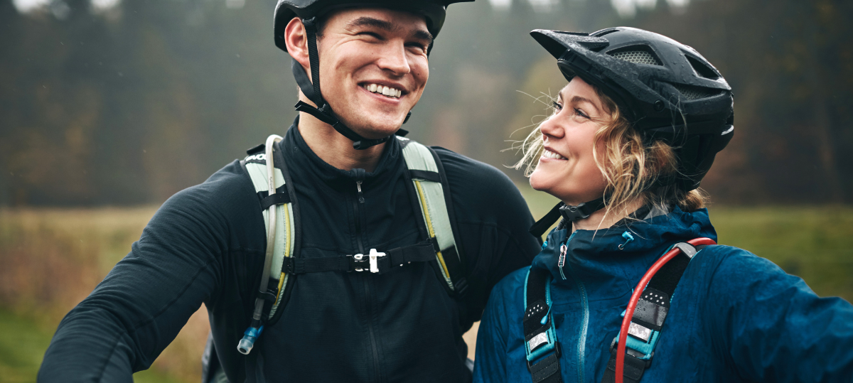 Man and woman smiling with bike helmets on outside