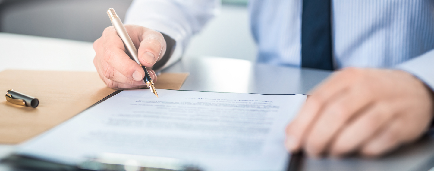 Person holding pen signing paper at desk